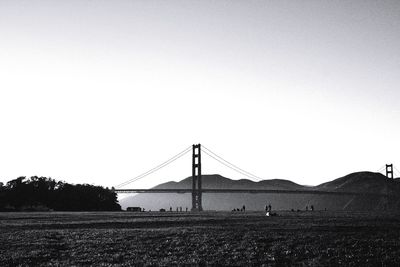 Suspension bridge over field against clear sky