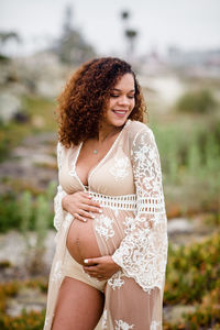 Young pregnant woman posing & smiling at beach in sheer dress