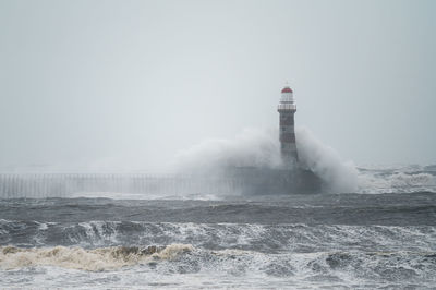 Lighthouse during stormy sea against clear sky
