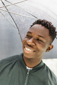 Young african american man under black umbrella in rain, smiling. fall or spring weather