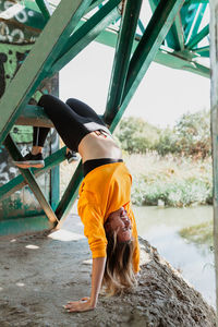 Full length of young woman exercising by railway bridge