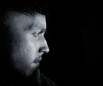 Side view of thoughtful serious young man looking away against black background