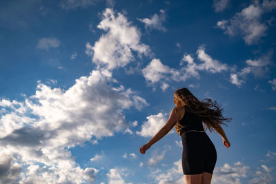 Low angle view of woman dancing against clouds in the blue sky 