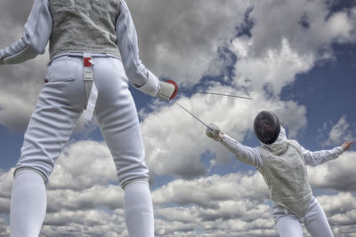 Low angle view of people fencing against sky