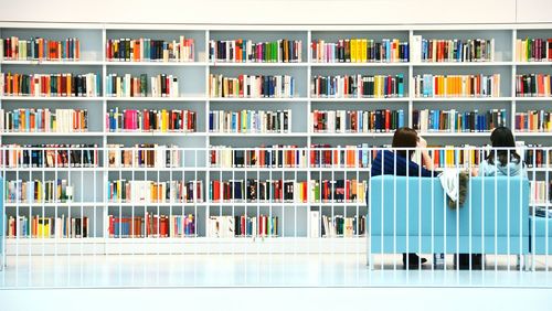 Rear view of people sitting on sofa in front of book selves at library