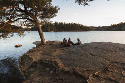 People sitting on rock by lake against sky