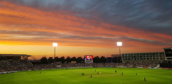 Group of people on soccer field against sky during sunset