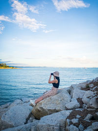 Girl on rock in sea against sky