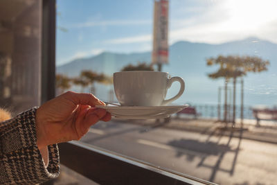 Cup of cappuccino held by a hand, with blurred lakefront in the background