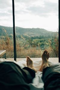 Low section of man relaxing on window against sky