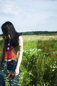 Rear view of woman with flowers on field against sky