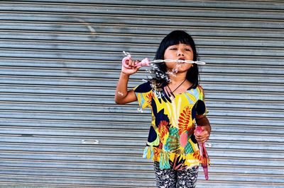 Side view of young woman blowing bubbles while standing against wall