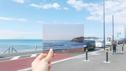 Person holding umbrella by sea against sky