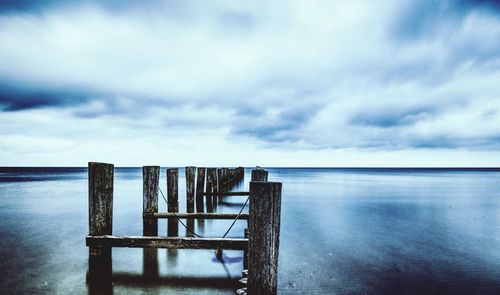 Wooden posts on pier over sea against sky