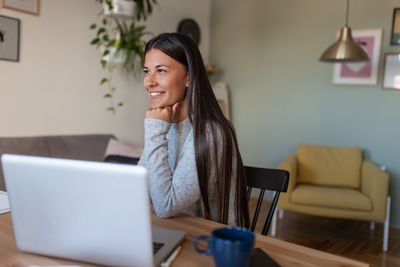 Young woman using phone while sitting on table at home