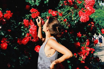 Side view of woman touching red flowers blooming outdoors