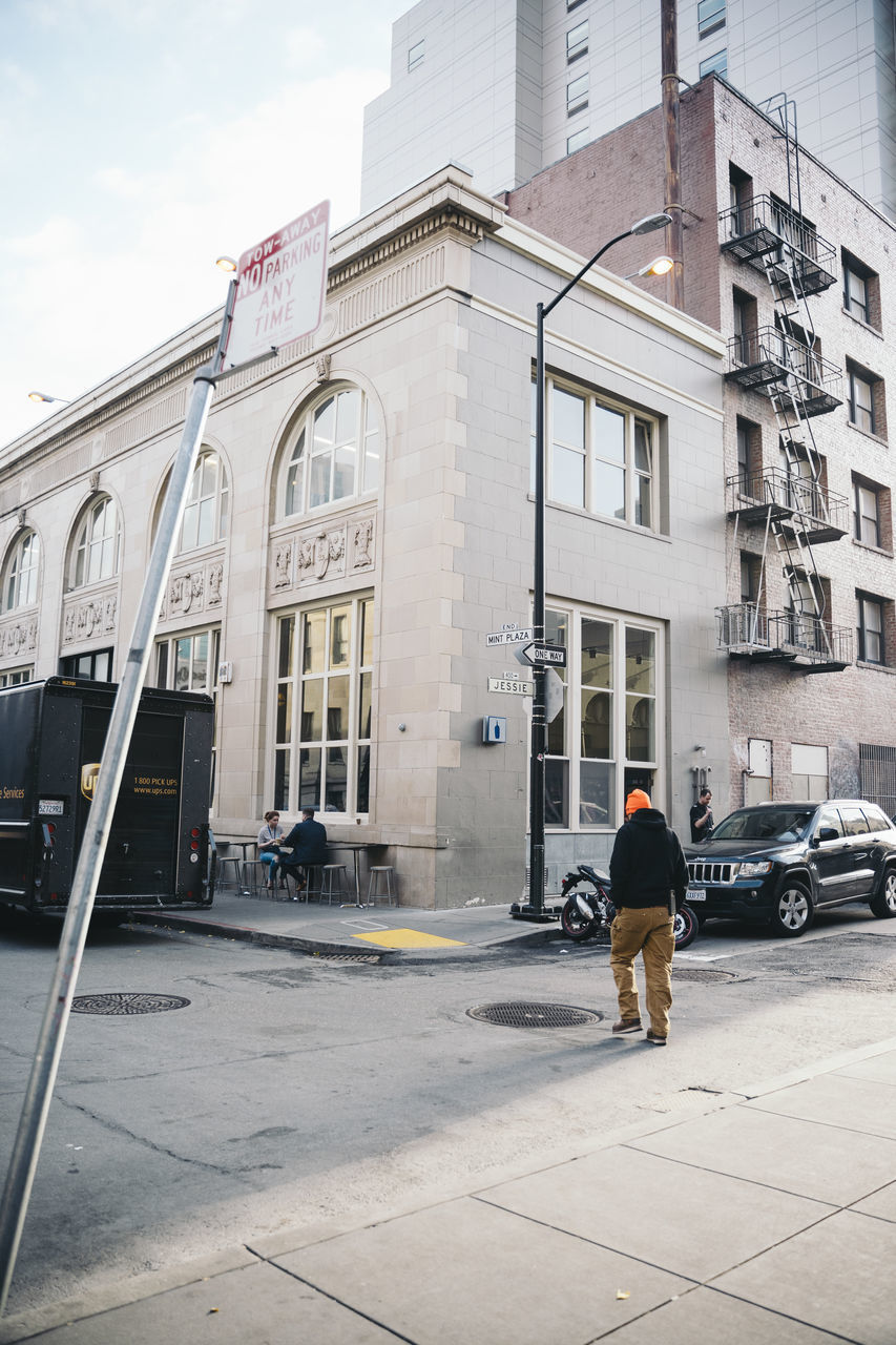 FULL LENGTH OF MAN WALKING ON STREET AGAINST BUILDING IN CITY