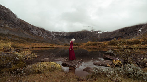 Woman standing on rock amidst mountains against sky