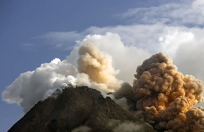 Low angle view of smoke emitting from volcanic mountain against sky