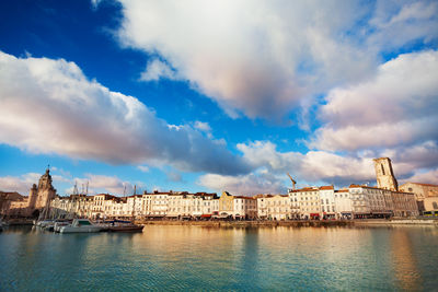 View of buildings by river against cloudy sky