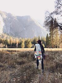 Rear view of woman carrying shawl on shoulder at grassy field against mountain