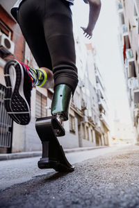 From below back view of young guy with leg prosthesis running during workout on city street