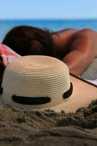 Close-up of hat with woman sleeping on sand in background