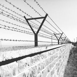 Barbed wire fence on retaining wall against sky