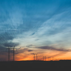 Silhouette of electricity pylons on field at sunset