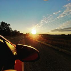 Road amidst field against sky during sunset