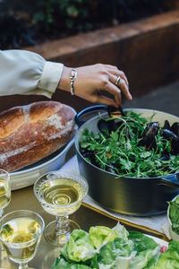 Women using hand to pick steamed mussels out of pot at dinner table with white wine, bread