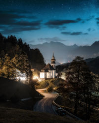 Illuminated building by trees against sky at night