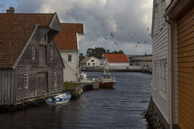 Houses by river amidst buildings against sky