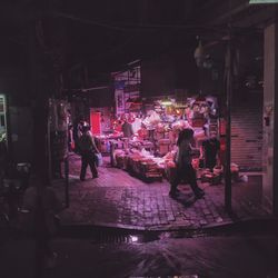 People at illuminated market on sidewalk in city during night