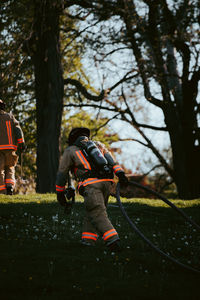 Rear view of firefighter dragging pipe