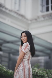 Portrait of smiling young woman standing against built structure