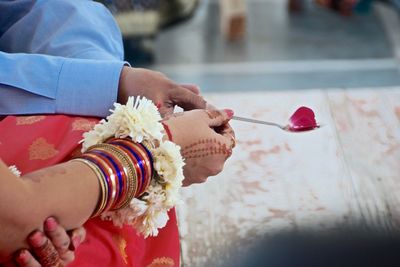 Cropped hands of bride and bridegroom holding spoon with petal