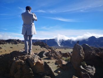 Rear view of man standing on rocks against sky