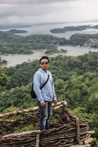 Portrait of young man standing on wood against sky