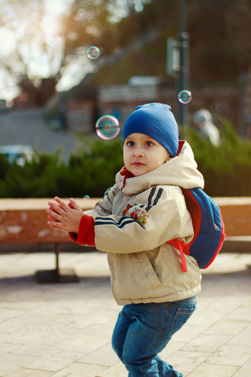 PORTRAIT OF CUTE BOY STANDING AGAINST BLURRED BACKGROUND