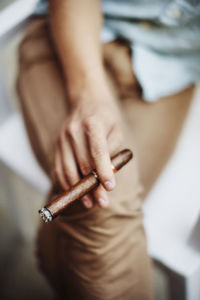 Close-up of man holding cigar while sitting on chair