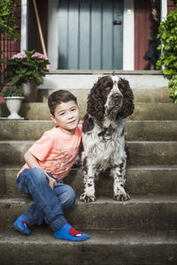 Portrait of smiling boy sitting with english springer spaniel on steps in back yard