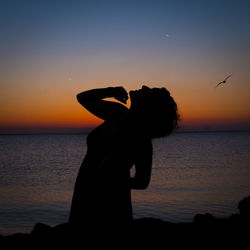 Silhouette woman standing by sea against sky during sunset