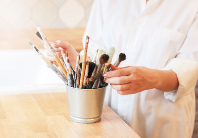 Midsection of woman arranging paintbrushes in jar on table