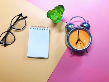 Directly above of eyeglasses with alarm clock and spiral notebook on colored background