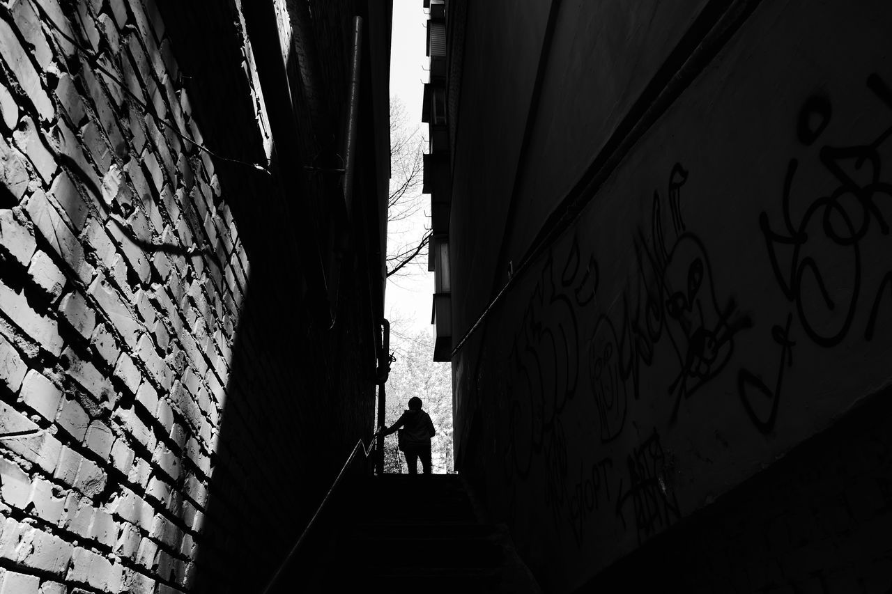 black, architecture, black and white, white, darkness, built structure, monochrome, monochrome photography, silhouette, light, building exterior, walking, city, wall - building feature, shadow, men, line, one person, lifestyles, day, low angle view, building, full length, outdoors, graffiti, adult, city life, sunlight, nature, standing