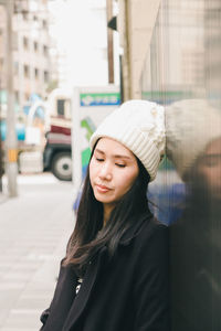 Thoughtful woman in knit hat standing by wall