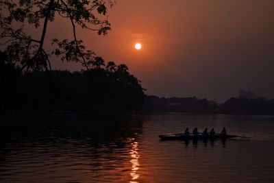 Silhouette people on lake against sky during sunset