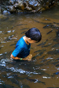 An asian boy feed and play with kelah fish in kelah sanctuary kenyir lake, terengganu.