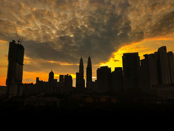 Silhouette of buildings against cloudy sky during sunset